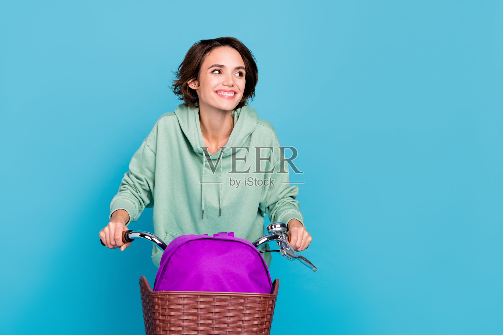 梦幻般的闪亮女性穿着绿色卫衣,骑自行车,背包空着,背景为蓝色。照片摄影图片
