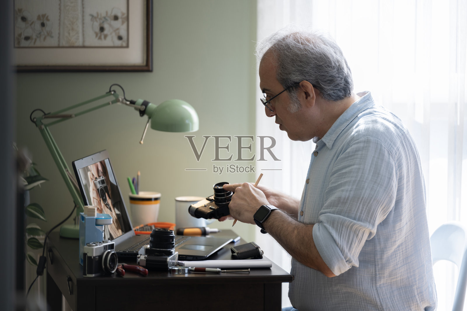 一名男子在家修理相机,并在电脑上查看说明。照片摄影图片