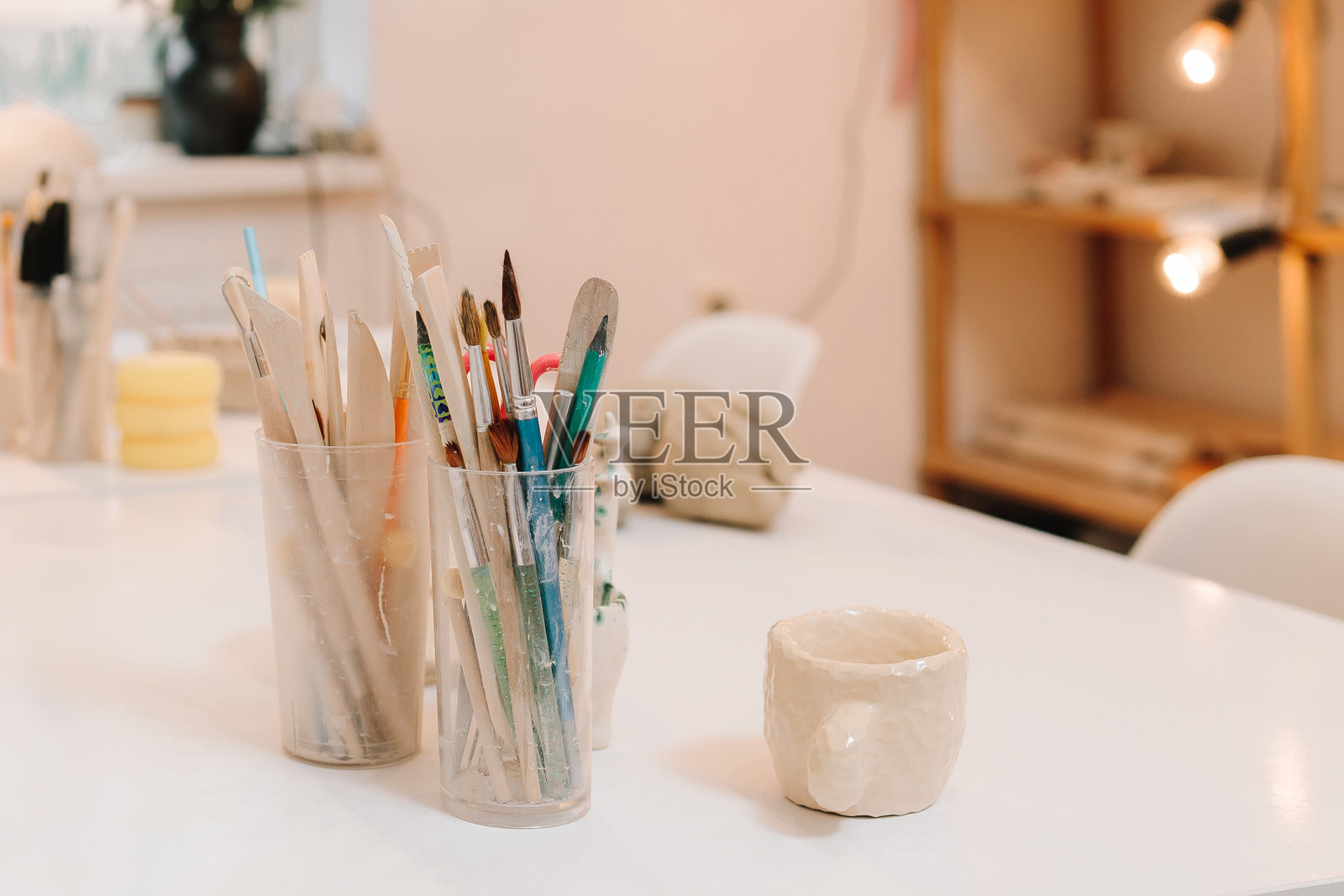 舒适的艺术工作室,配有雕刻工具。创造性的氛围,适合设计陶瓷器皿,桌上有画笔和手工陶瓷杯。照片摄影图片