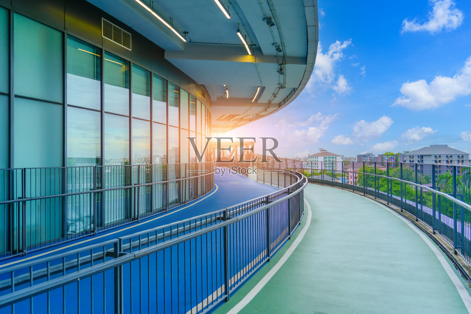 长长的绿色步道在混凝土建筑之间延伸,阳光照耀下适合运动健身的拉伸。环境将城市建筑与自然元素融合,靠近住宅区。照片摄影图片