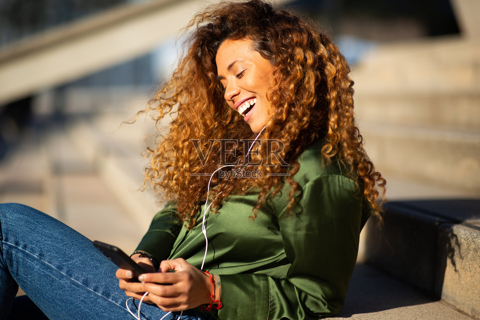 时尚的拉丁女性在城市楼梯上通过手机和耳机听音乐照片摄影图片
