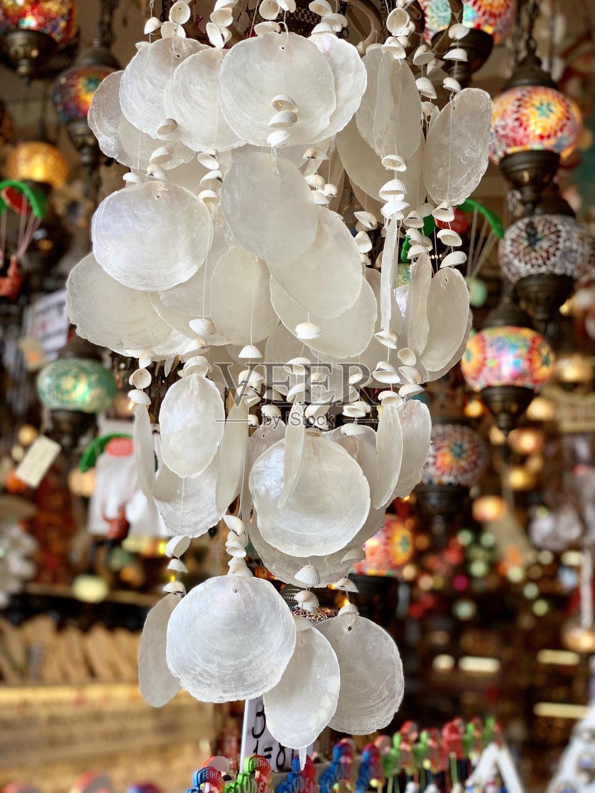 美丽的贝壳风铃悬挂在充满活力的市场环境中,周围是五彩斑斓的马赛克灯笼。精致的细节为市场增添了魅力和创意感。照片摄影图片