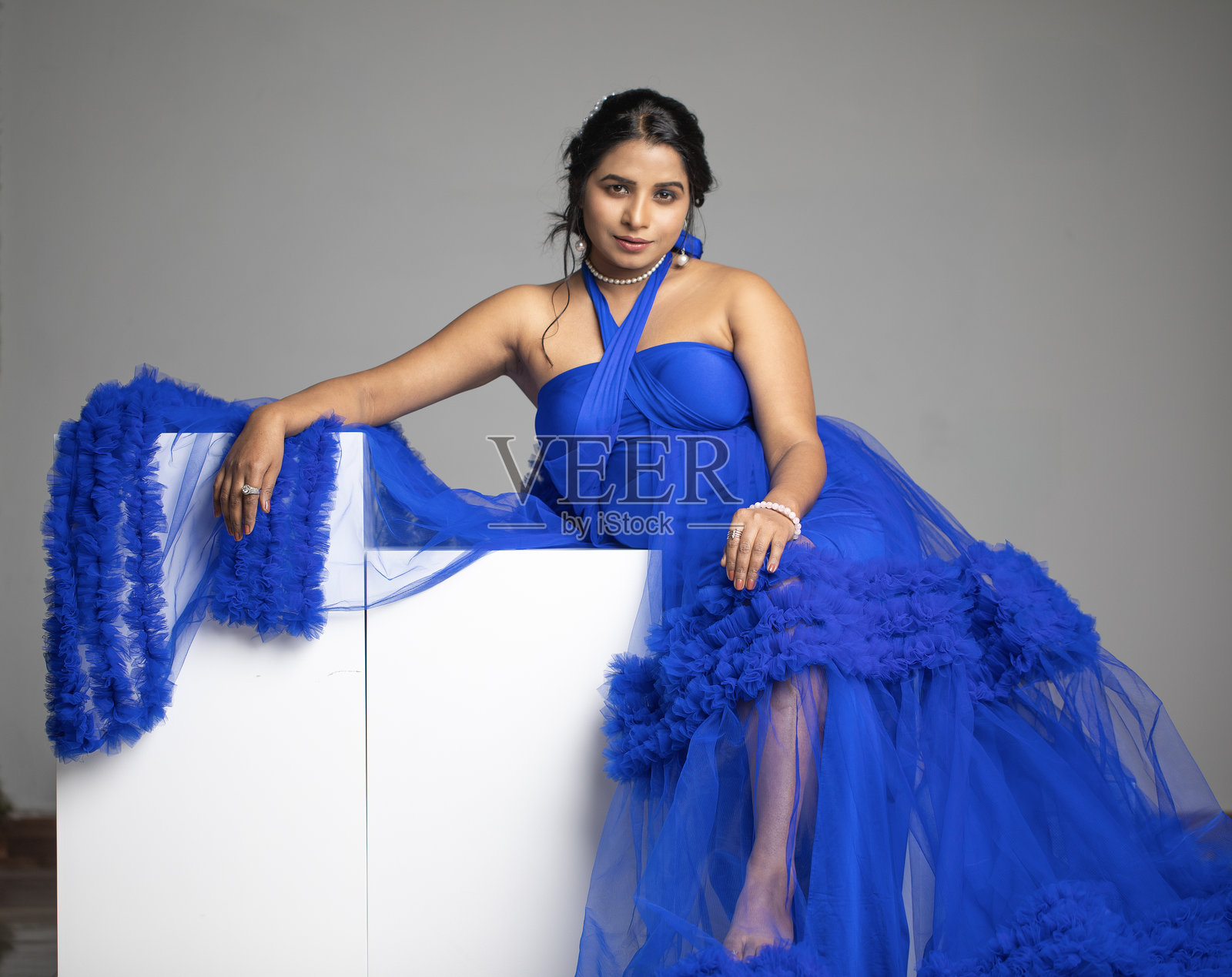 穿着优雅蓝色连衣裙的女性在灰色背景前摆姿势照片摄影图片
