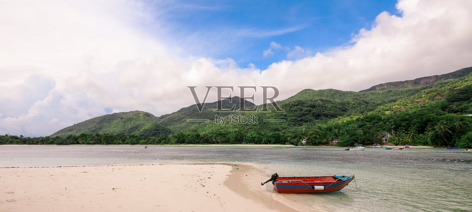 塞舌尔宁静的海滩上,一只孤独的小船静静地停靠在岸边,背景是郁郁葱葱的山脉。照片摄影图片