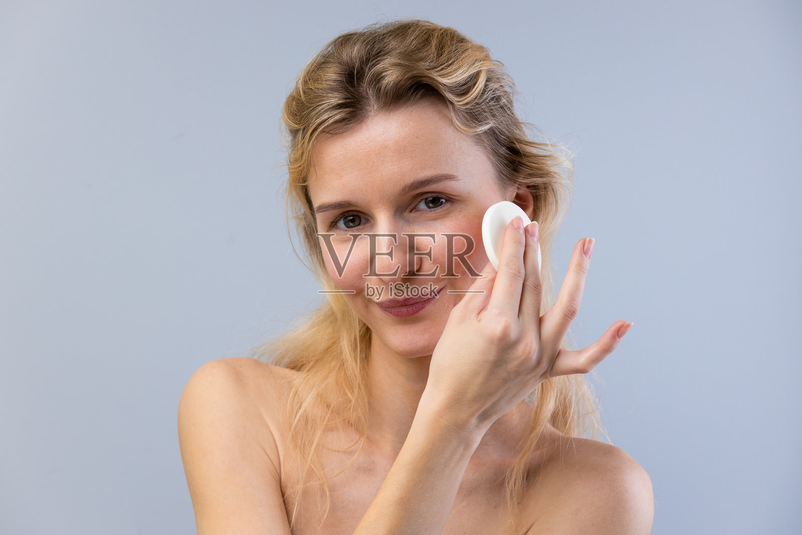 自然护肤程序:光彩照人的女性在简约环境中使用棉垫涂抹面部产品,展现清新水润的肤色照片摄影图片