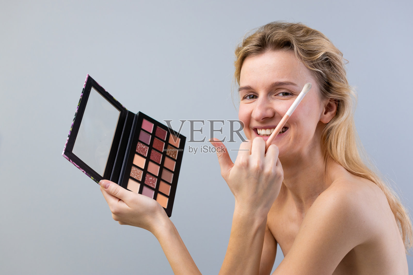 一位面带笑容的年轻女性手持色彩鲜艳的化妆盘和刷子,展现出她对化妆和现代美容创意的兴奋。照片摄影图片