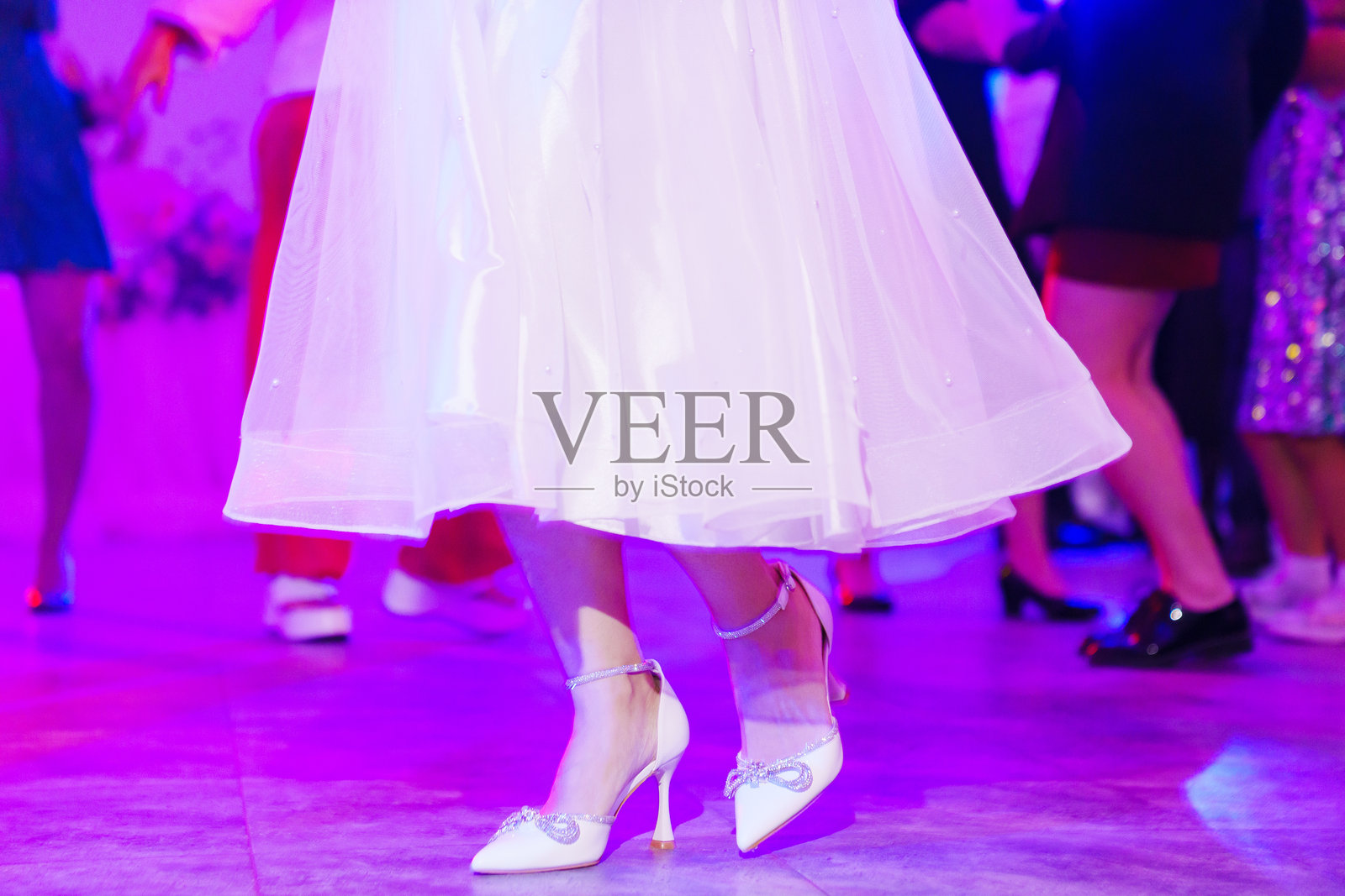 穿着白色鞋子和裙子的女性脚在舞池上跳舞。照片摄影图片