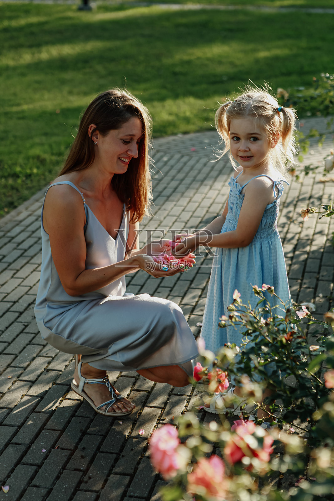 一位母亲和她的小女儿在公园里共享快乐时光。她们被五彩缤纷的花朵和郁郁葱葱的绿树环绕,营造出宁静的氛围。照片摄影图片