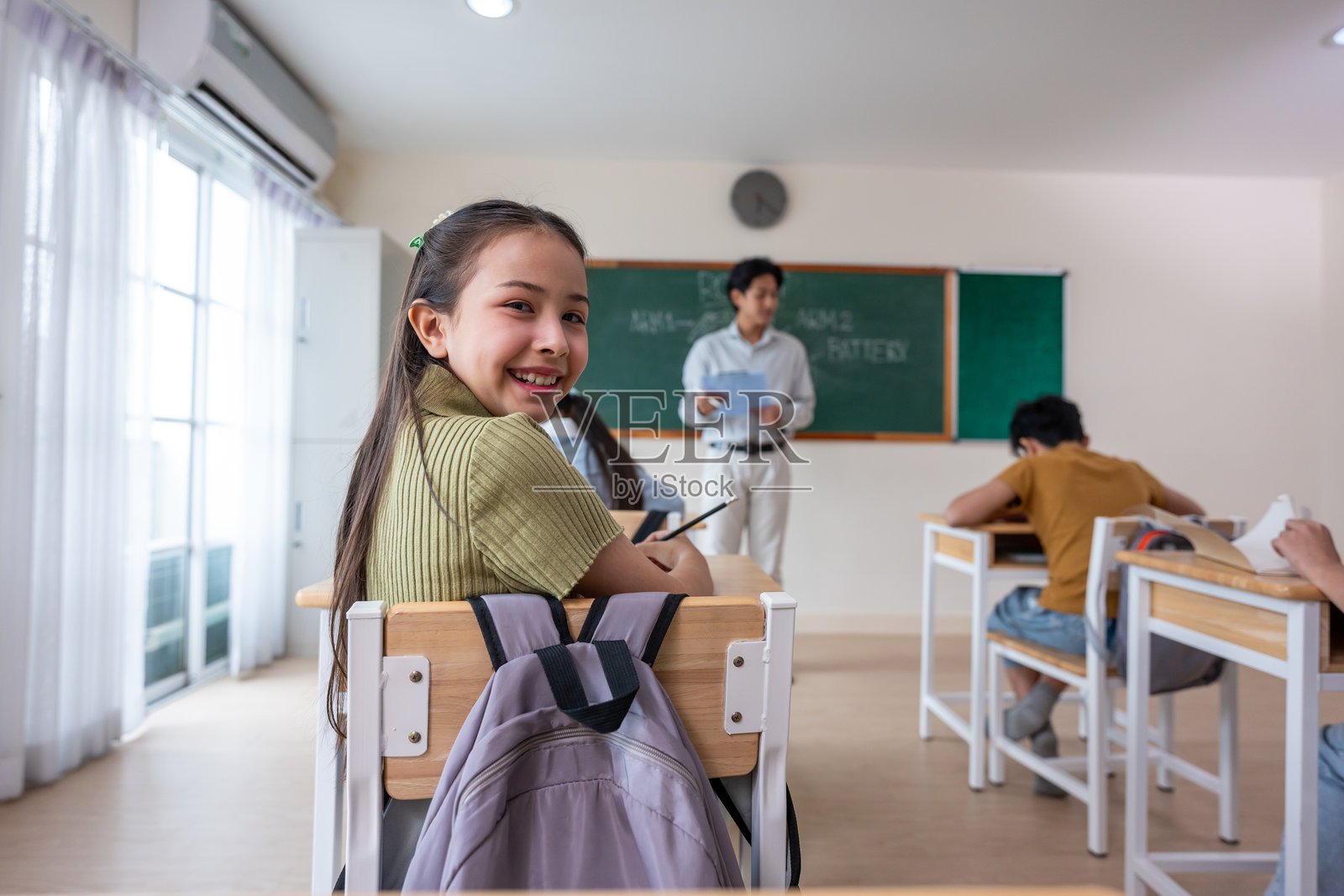 亚洲小女孩在小学教室里学习的肖像。可爱的年轻学生坐在学习桌上,认真听老师讲课,然后微笑着看向镜头。照片摄影图片