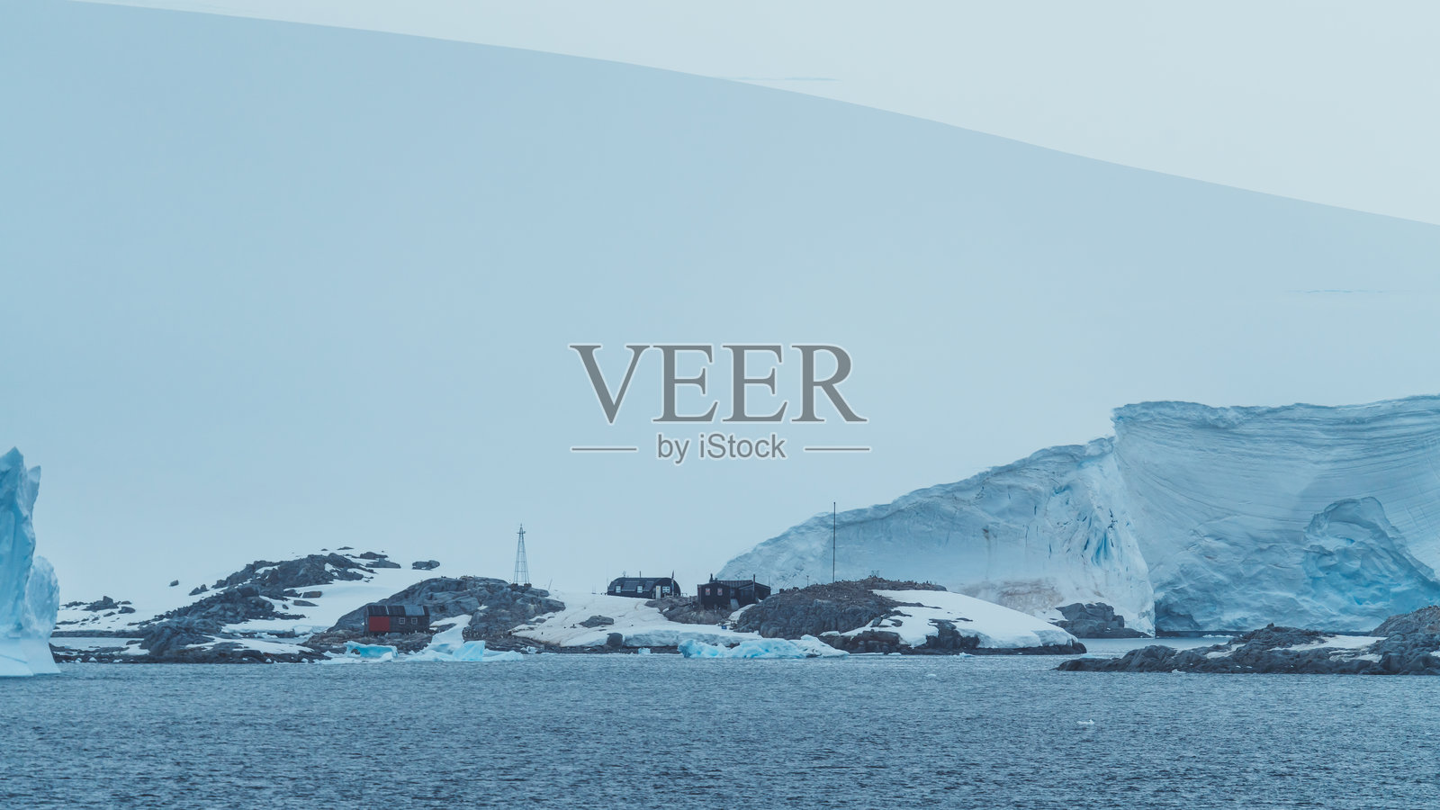 南极科学研究站在纽迈耶尔海峡的视角,从游轮上俯瞰岩石海岸,背后是覆盖着厚雪的冰架山脉。照片摄影图片