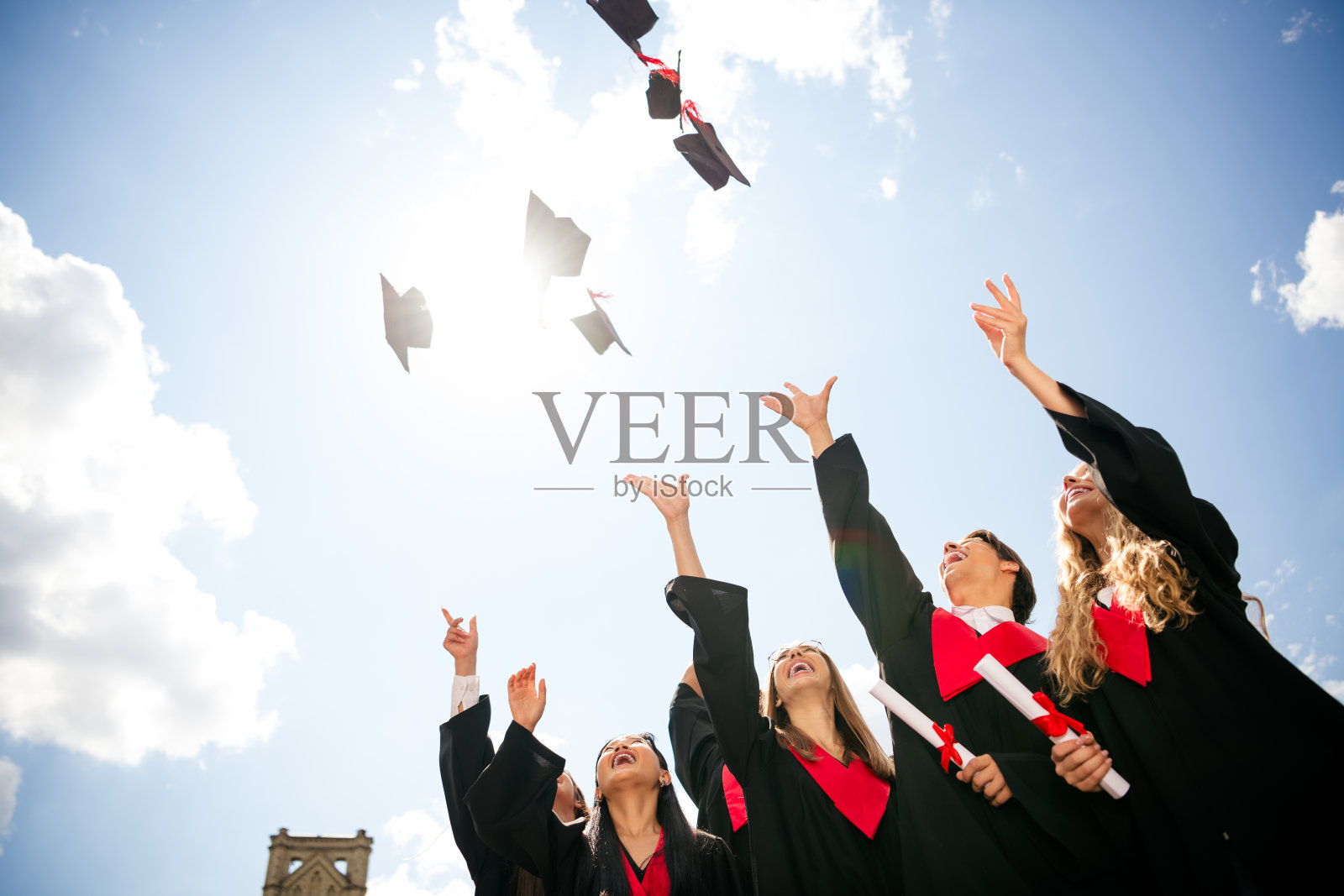 毕业生们在阳光明媚的天空中欢庆,抛洒学位帽,捕捉户外成就的快乐时刻。照片摄影图片