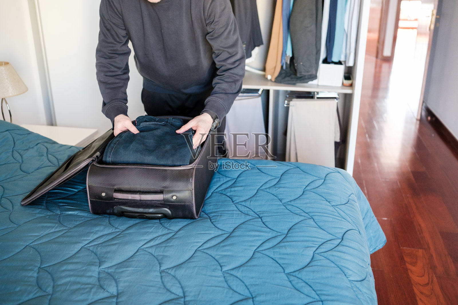 男子在酒店房间的床上将衣物打包进行李箱照片摄影图片