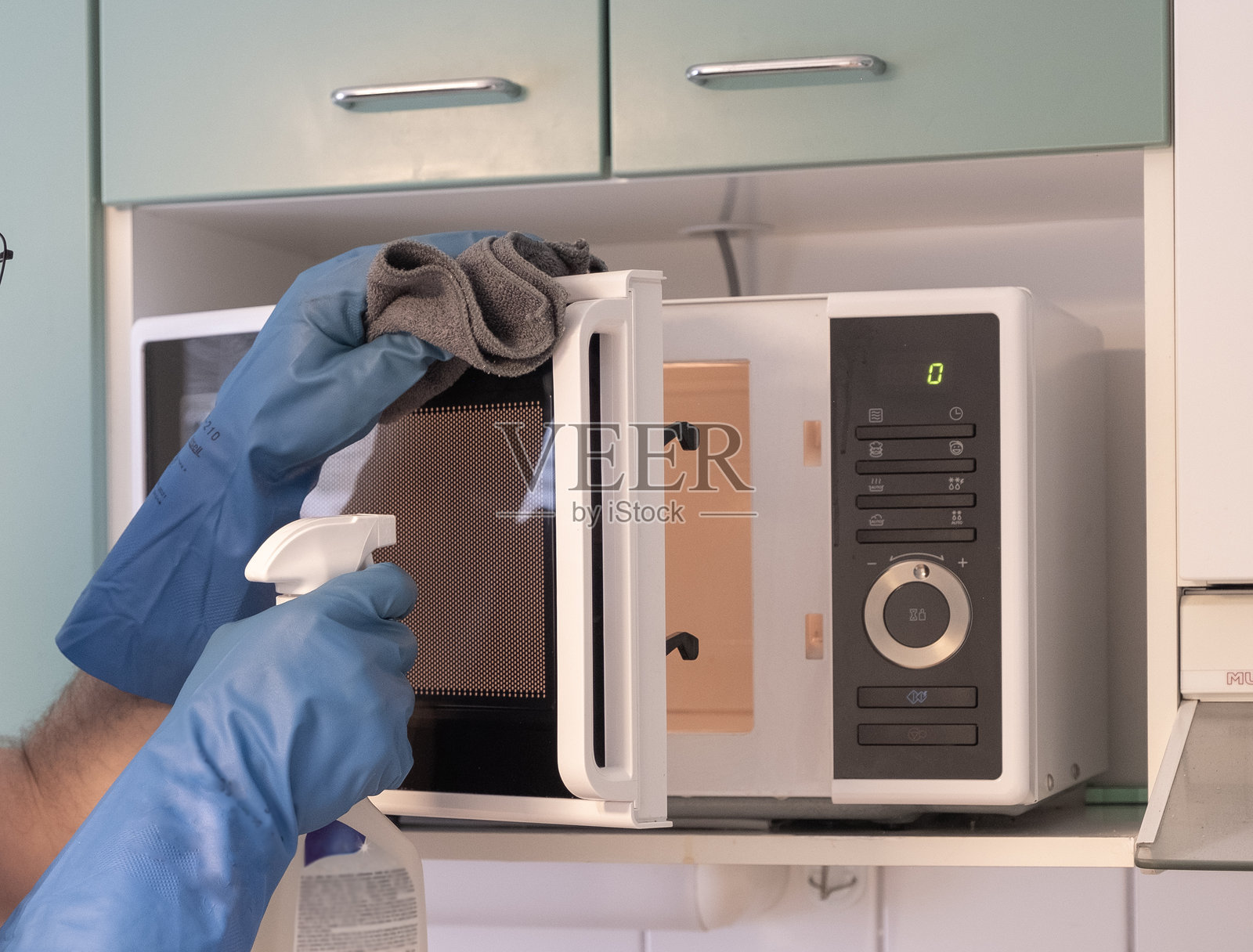清洗微波炉,戴着橡胶手套的人手。照片摄影图片