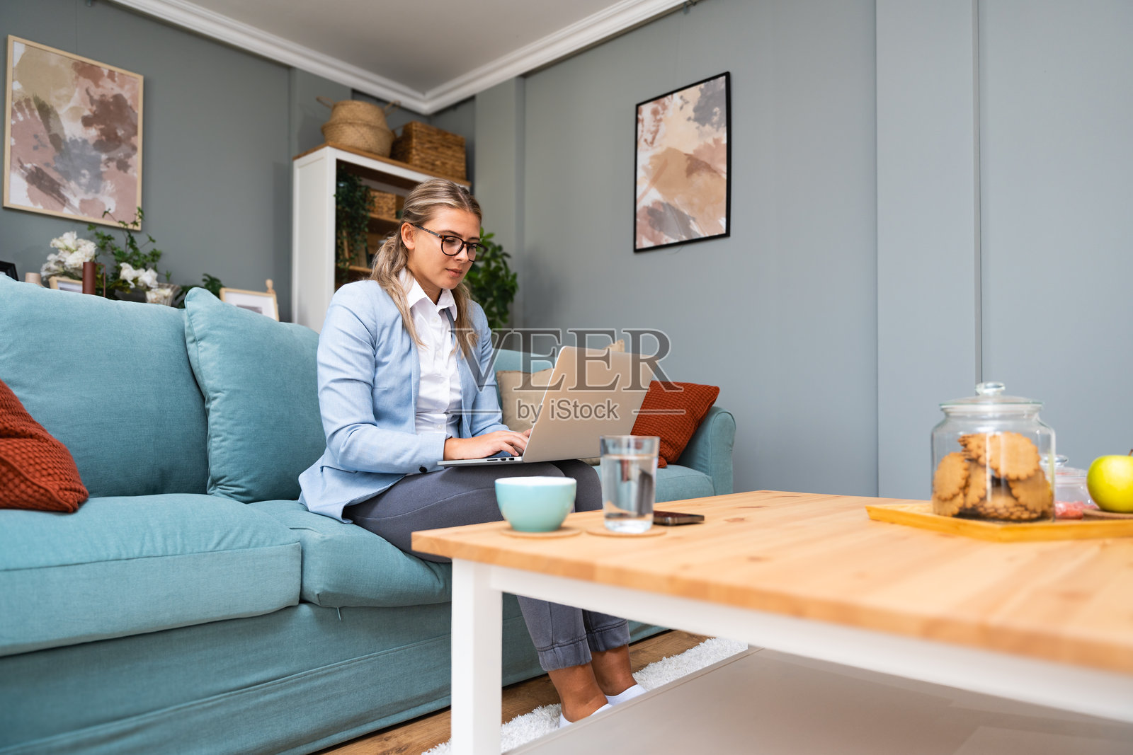 年轻漂亮的女商人在家办公室的沙发上躺着,使用笔记本电脑在线工作,进行视频通话。创意女性微笑着,查看社交媒体,发送信息。照片摄影图片