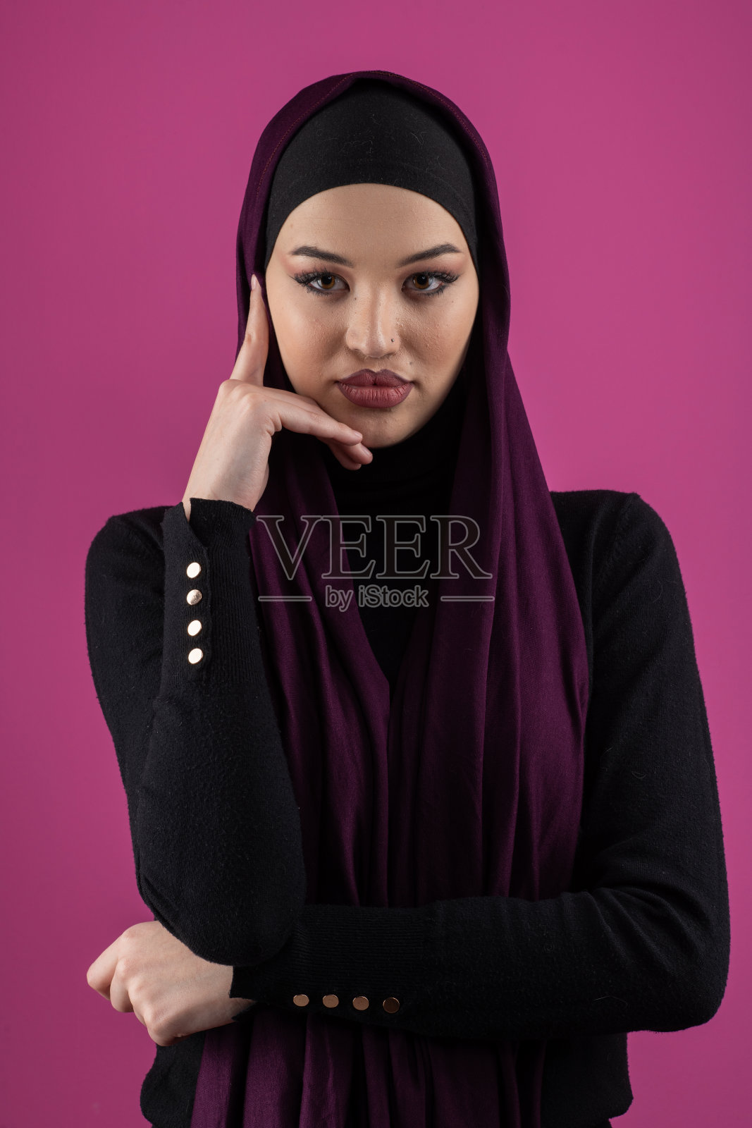优雅地在粉色背景的摄影棚中摆姿势的美丽穆斯林女性,佩戴着头巾。照片摄影图片