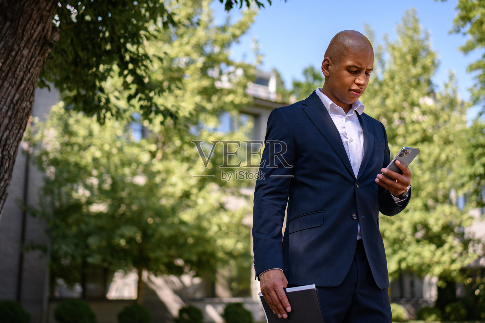 非裔美国商人在街上使用智能手机并手持文件。照片摄影图片