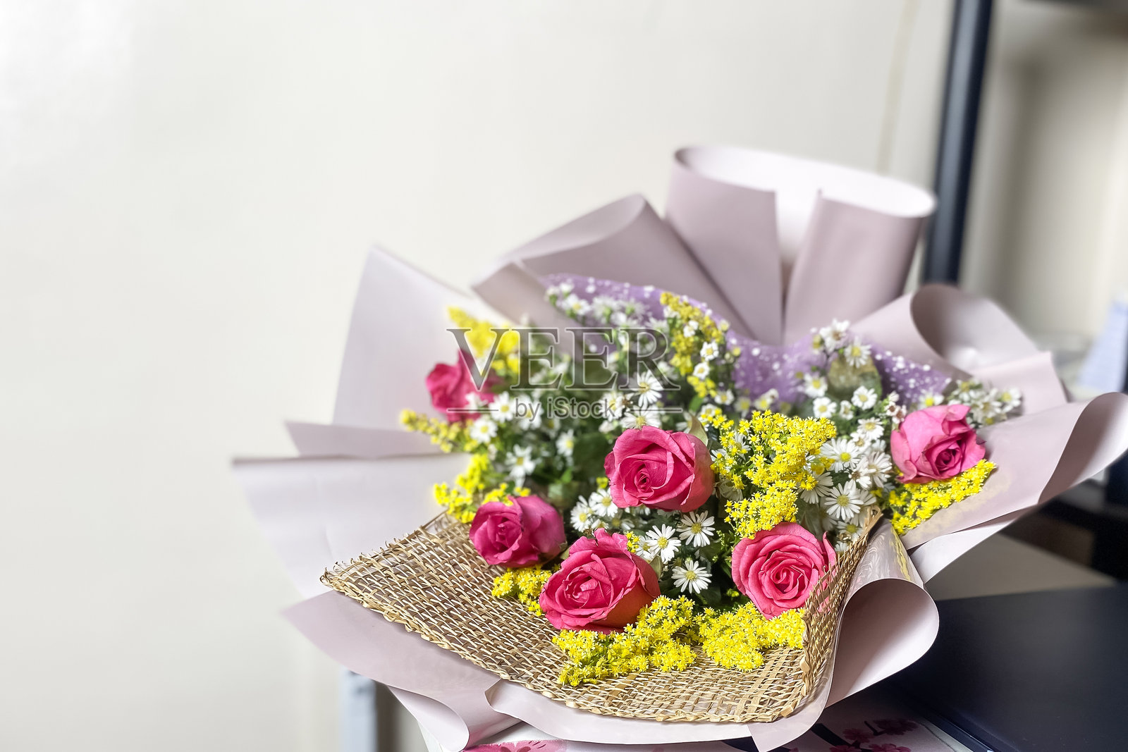 精致的花束,紫色纸包裹的玫瑰,搭配黄色小花,放在办公室的桌子上。照片摄影图片