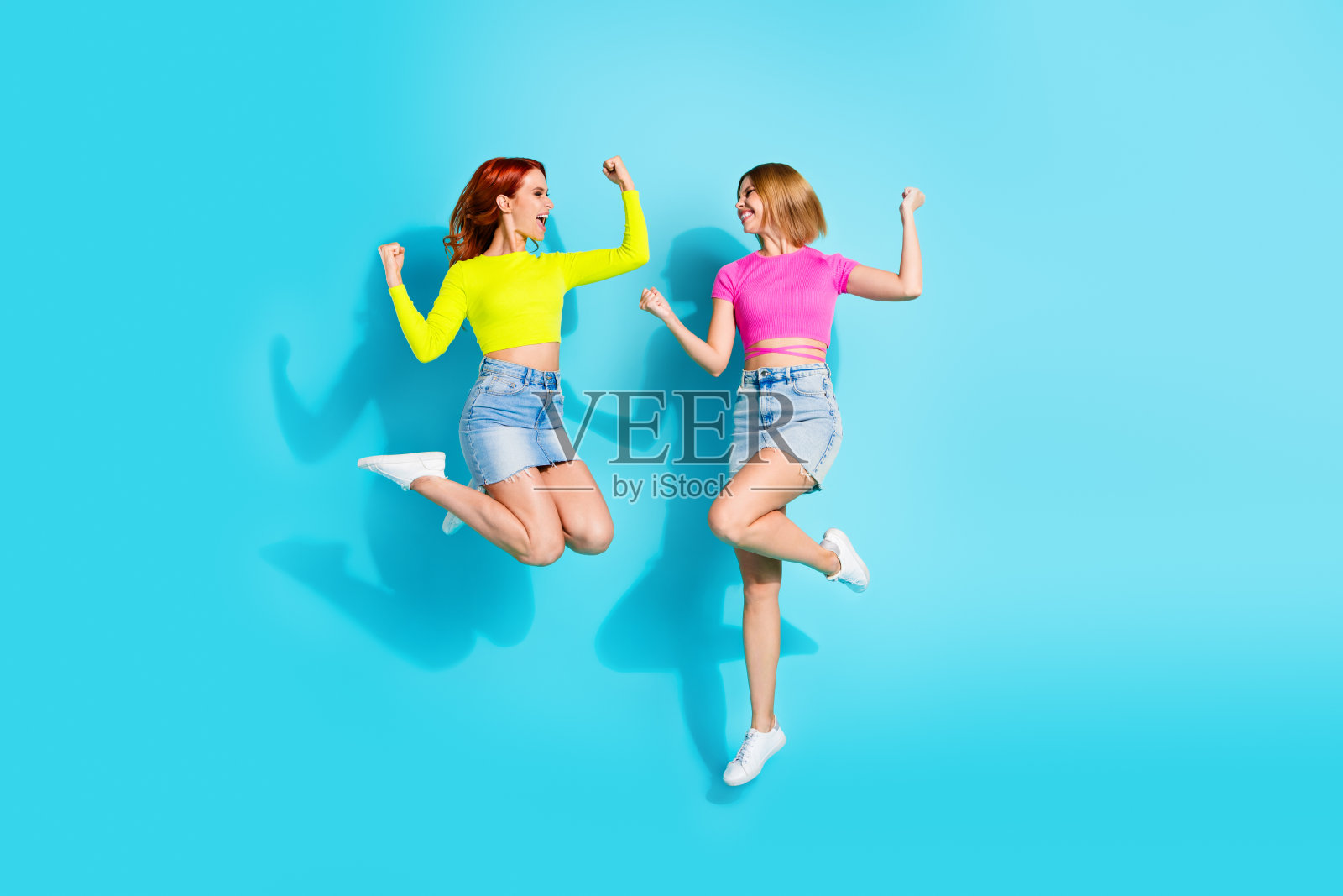 充满活力的年轻女性在青绿色背景上欢快地跳跃,展示时尚潮流和生动的表情。照片摄影图片