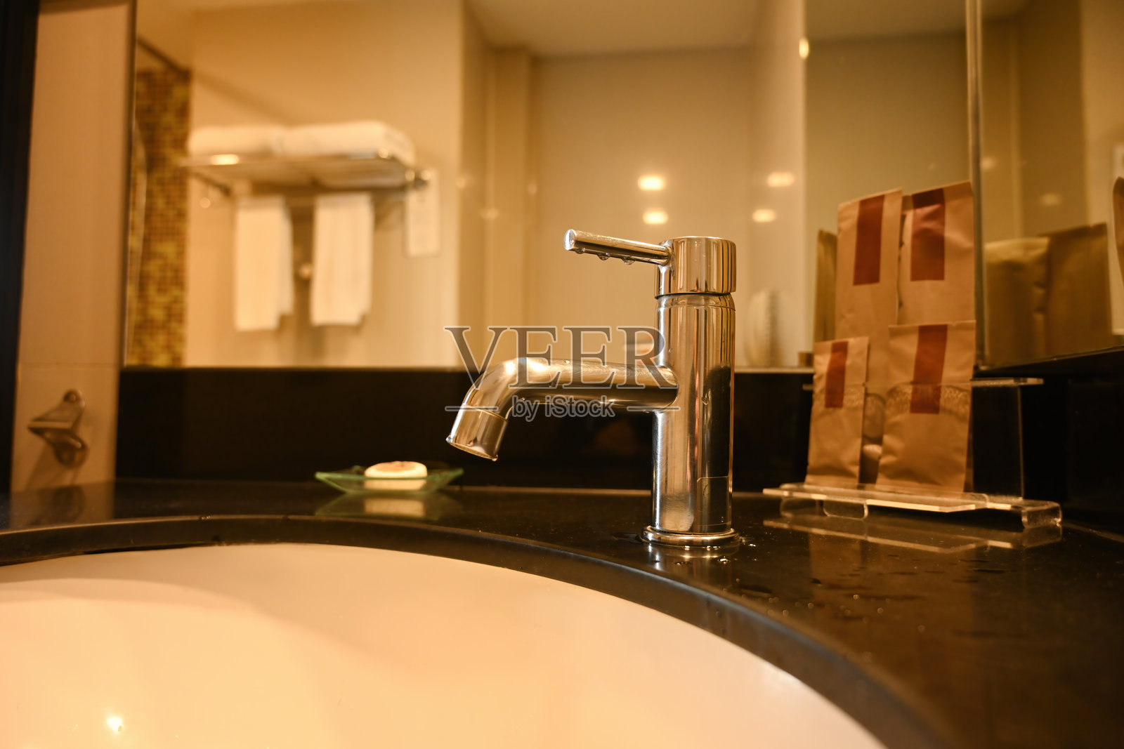 现代酒店浴室洗手池,光滑的黑色台面上配有抛光铬水龙头,镜子映照出毛巾和洗漱用品,展现出干净现代的酒店浴室风格。照片摄影图片