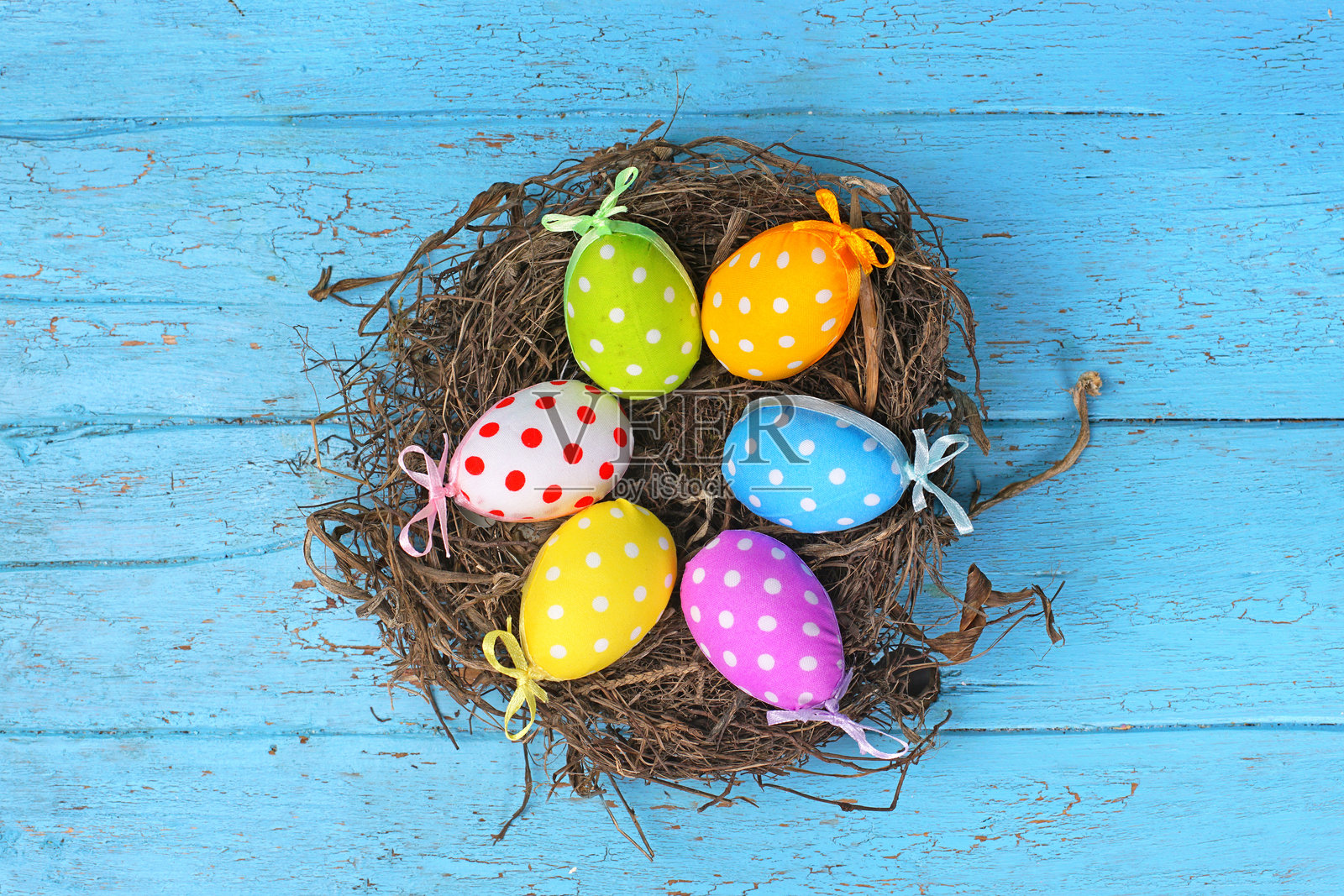 一个自然的鸟巢,里面放着五彩缤纷的复活节彩蛋,背景是蓝色木板。照片摄影图片