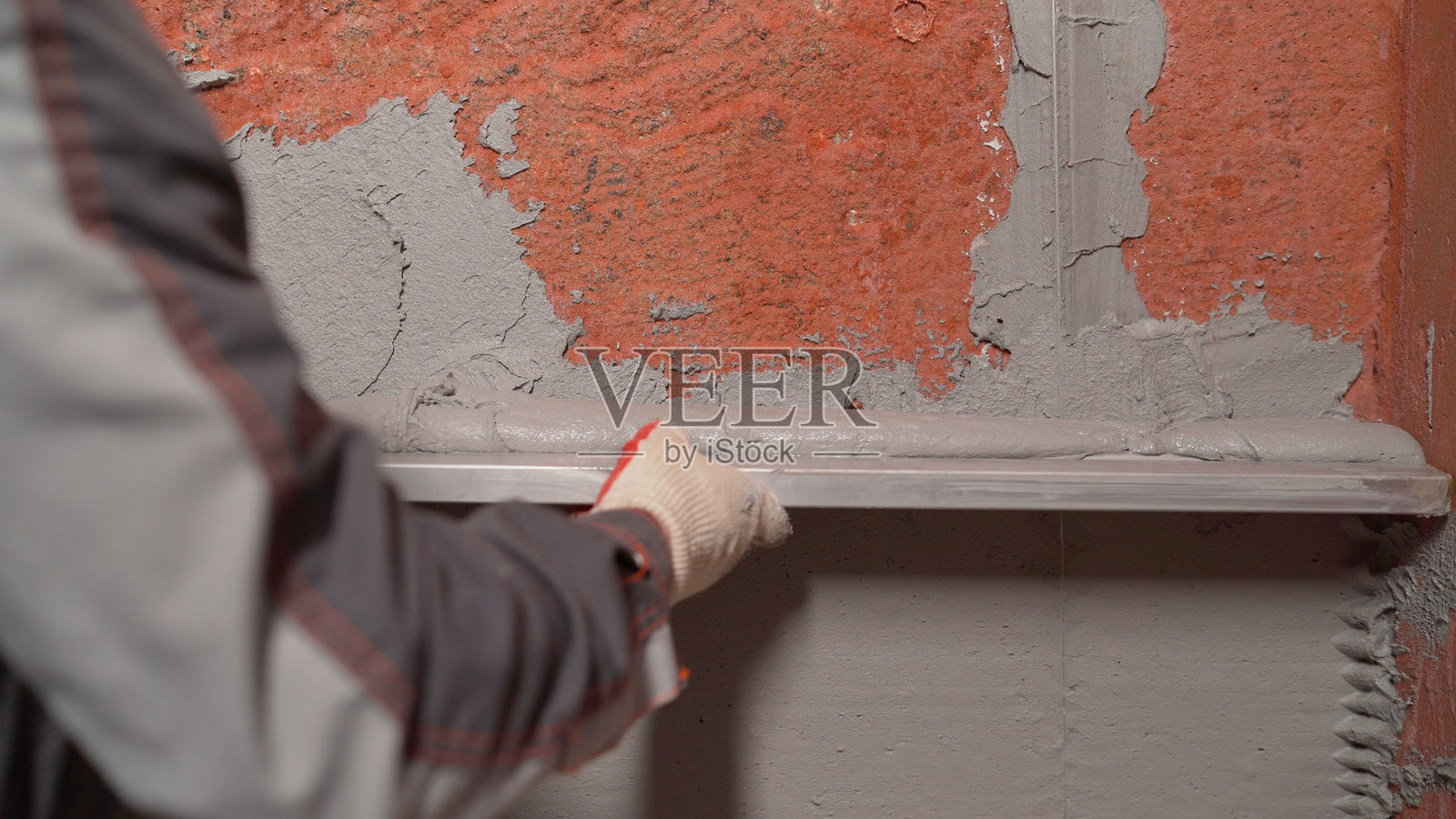 用刮刀在墙上抹灰。内部施工和装修工作。工人在墙上涂抹灰泥。手握建筑混合料的抹子,平整墙面。修补墙壁。用建筑工具抹平腻子。照片摄影图片