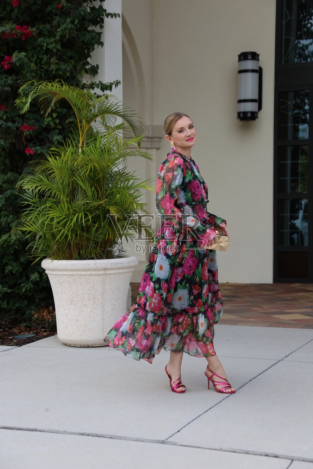 年轻美丽的女性穿着印花长裙,手提金色手袋。照片摄影图片