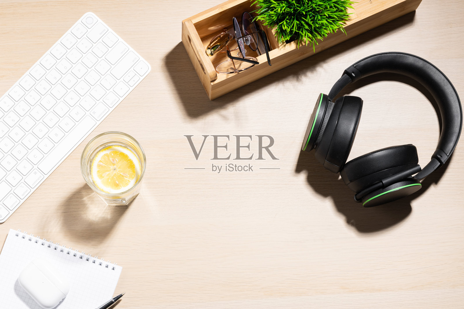 一杯清水装在透明玻璃中,旁边有一片柠檬,放在浅色木桌上。附近是一台白色的电脑键盘。办公室环境,暗示着一个清新的休息时刻或在工作期间保持水分的尝试。照片摄影图片