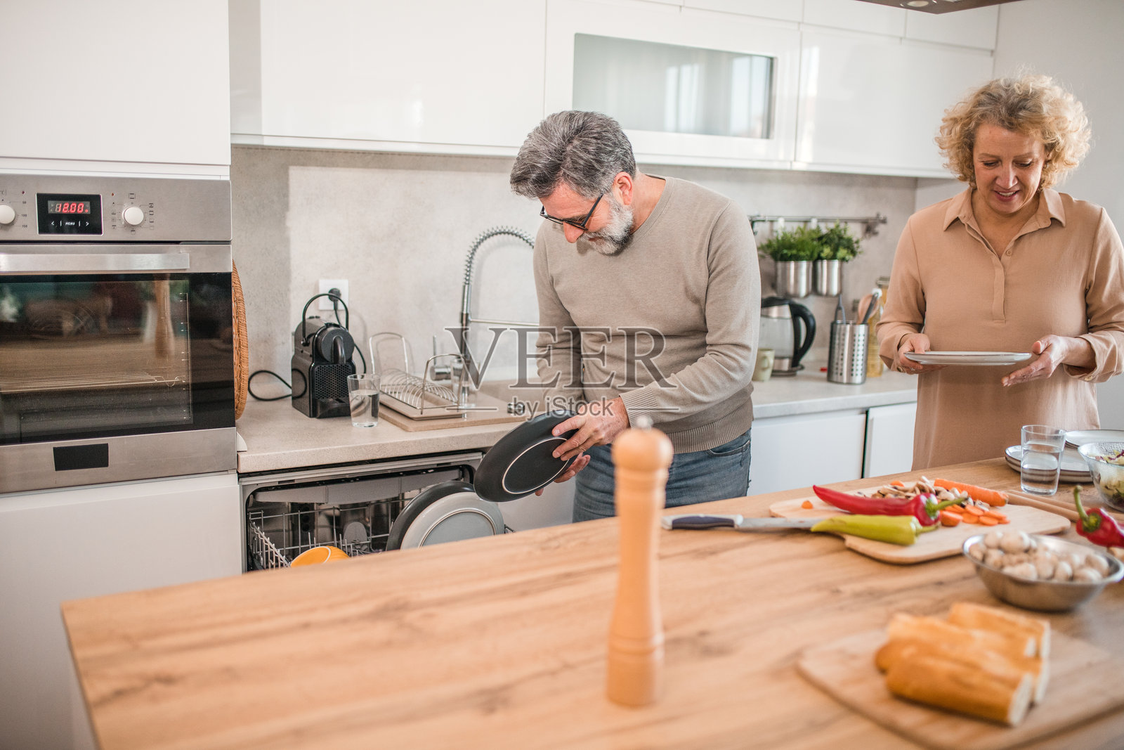 一名男子在与妻子准备午餐后,将脏盘子放入洗碗机。照片摄影图片