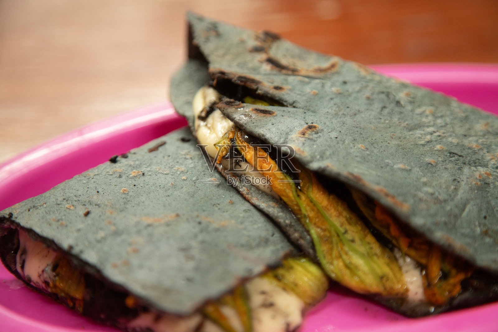 在墨西哥普埃布拉的乔卢拉市场上,使用紫玉米在传统的烤盘上制作的南瓜花和奶酪玉米饼。照片摄影图片