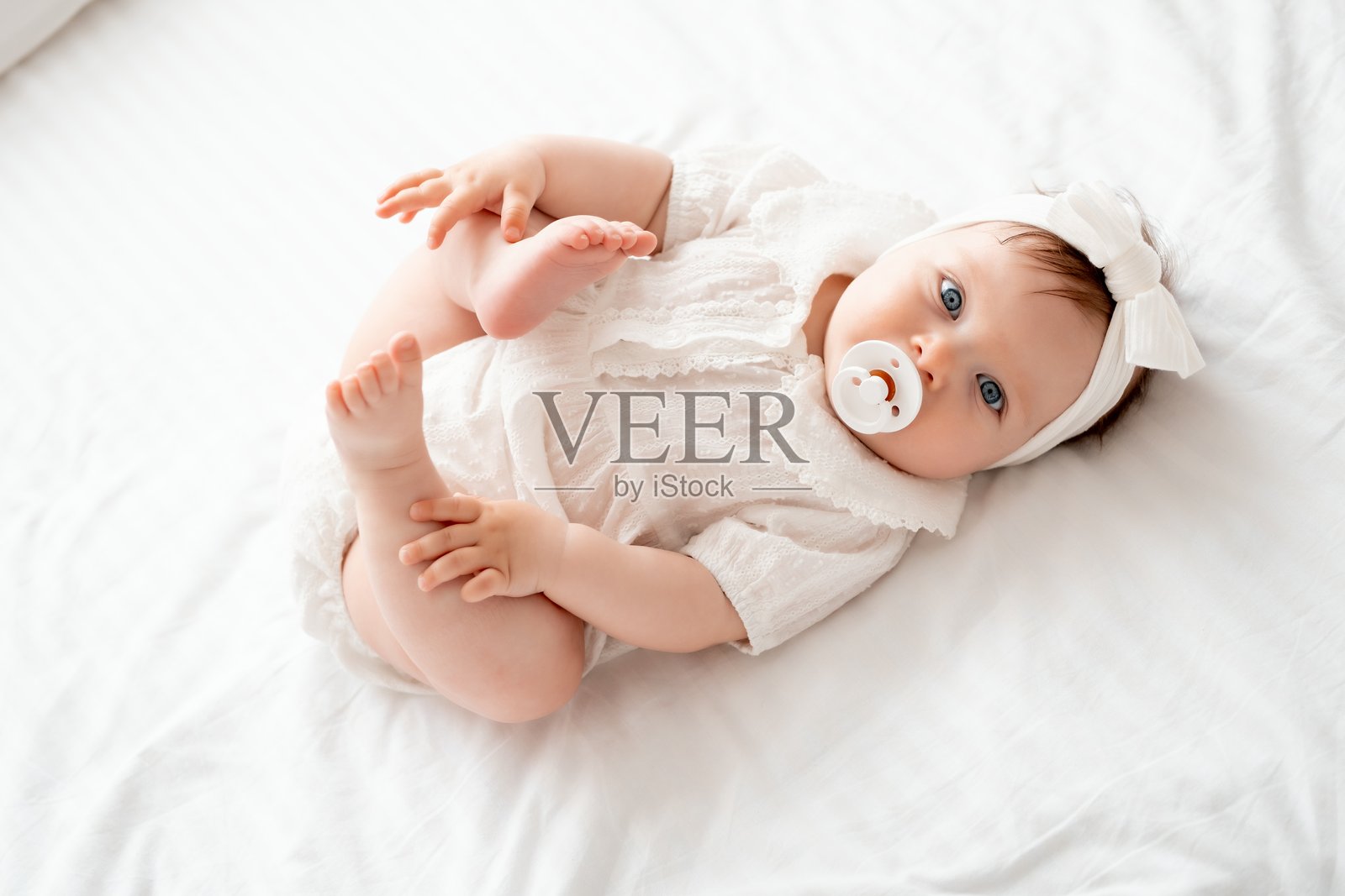 可爱的婴儿女孩穿着白色衣服,仰卧在家里的床上吮吸奶嘴,宝宝可爱地躺着,留有文字空间。照片摄影图片