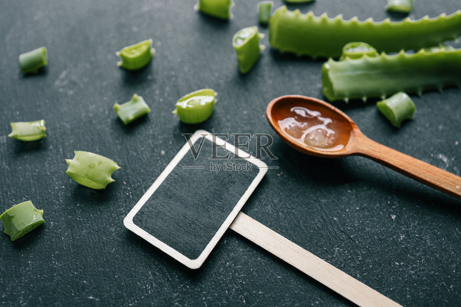 新鲜的芦荟叶、切好的片和木勺中的凝胶,背景为黑色,旁边有一个空白的黑板标志。自然护肤、健康和美容概念。照片摄影图片