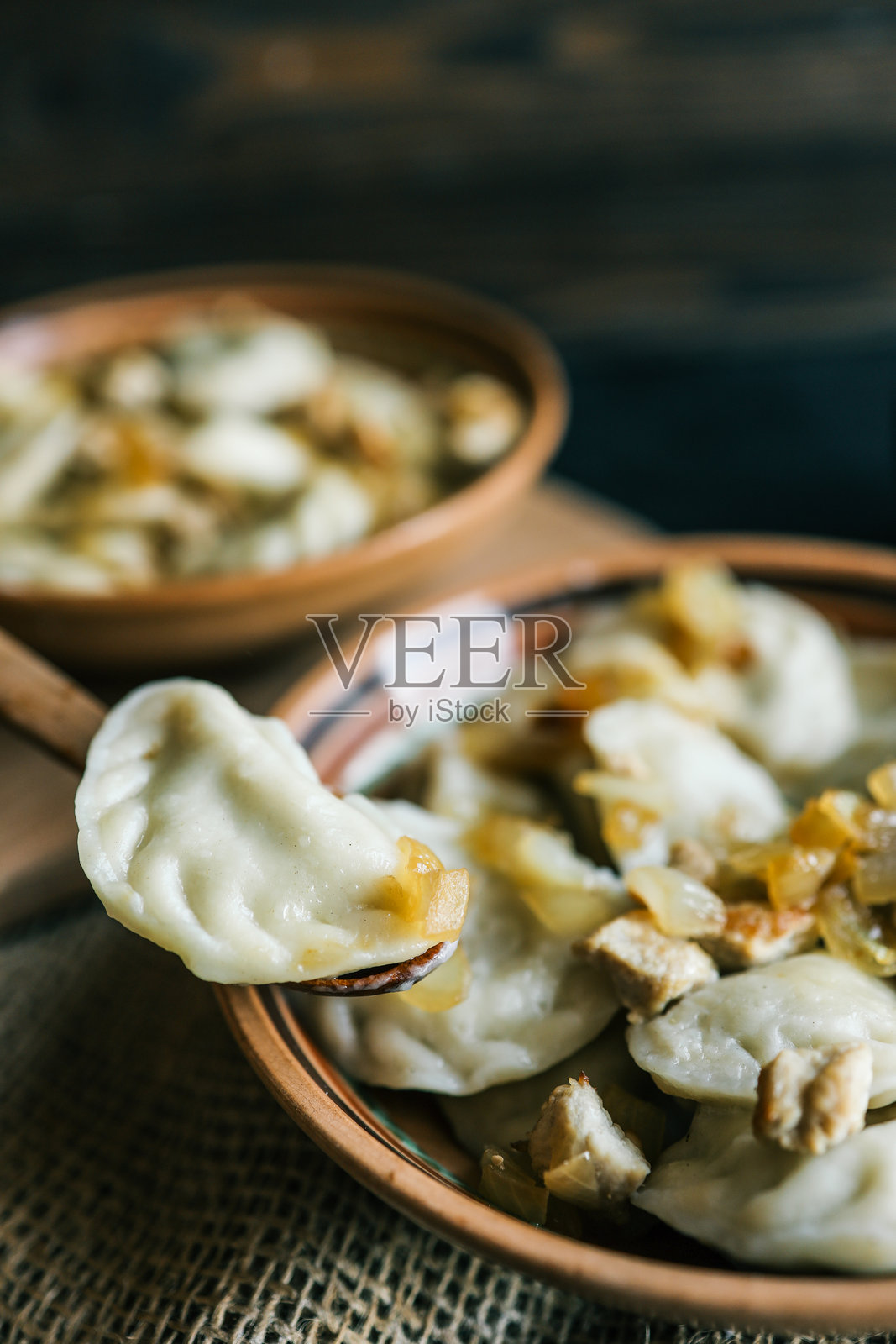 传统饺子的特写,配有炒洋葱和肉,盛放在陶瓷碗中,放在质朴的麻布上,一个饺子放在木勺上。照片摄影图片