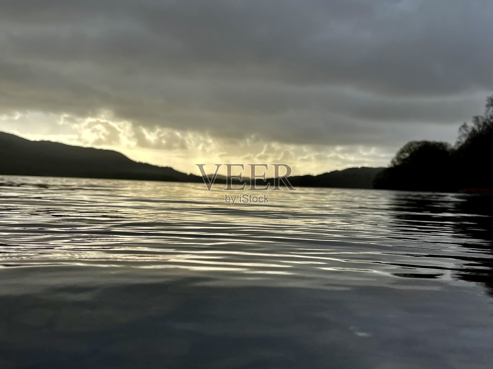 日落时分宁静的湖泊,波光粼粼的水面,剪影般的山丘和戏剧性的云彩照片摄影图片