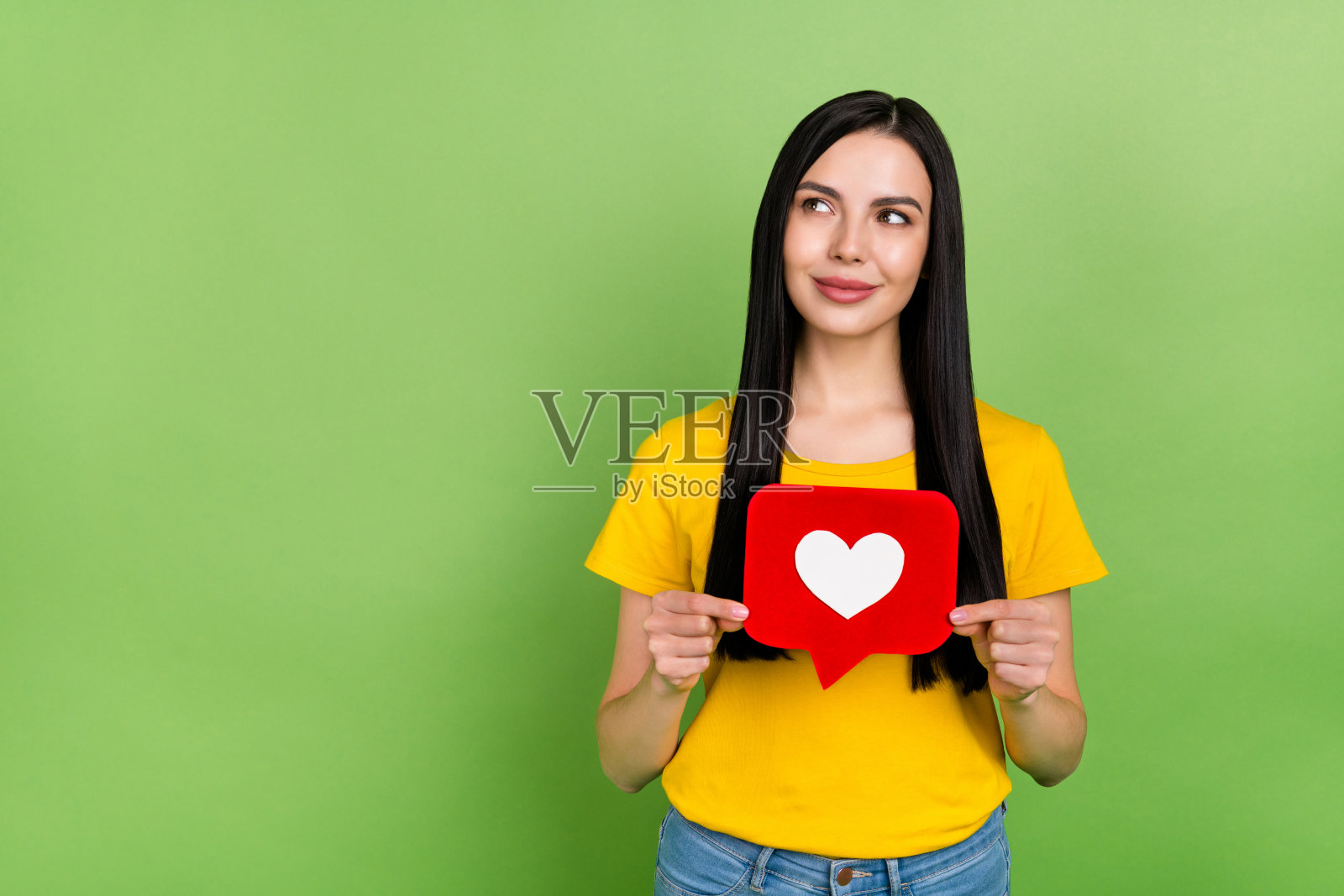 穿着黄色T恤的快乐梦幻女孩手持心形标志,背景为空白的绿色。照片摄影图片