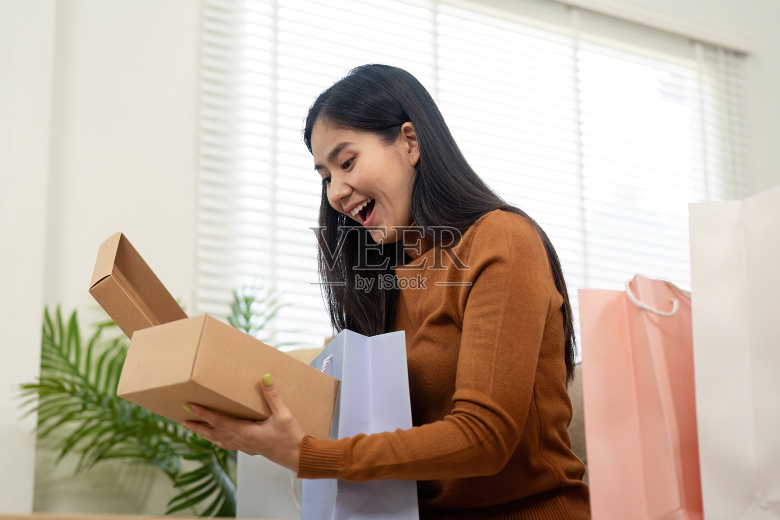 开箱的兴奋。女人快乐地打开一个包裹,周围是购物袋。照片摄影图片