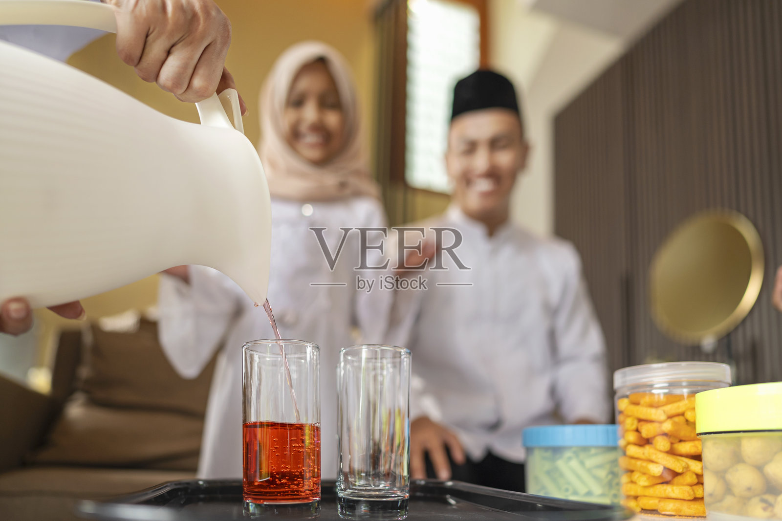 印尼穆斯林母亲在庆祝开斋节时为全家人端饮料的肖像。快乐的开斋节、开斋节、伊杜尔·菲特里和斋月庆祝的概念。照片摄影图片