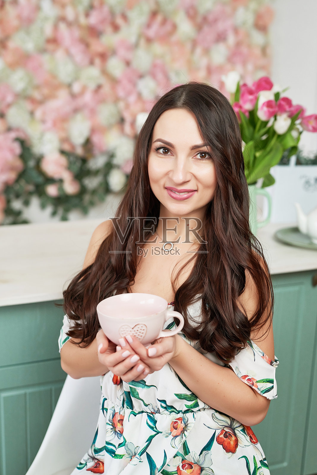 美丽的女孩手持杯子,背景是花卉图案。适合3月8日国际妇女节或母亲节的贺卡。非常漂亮的女性,背景是五彩缤纷的盛开花朵。女性肖像。照片摄影图片