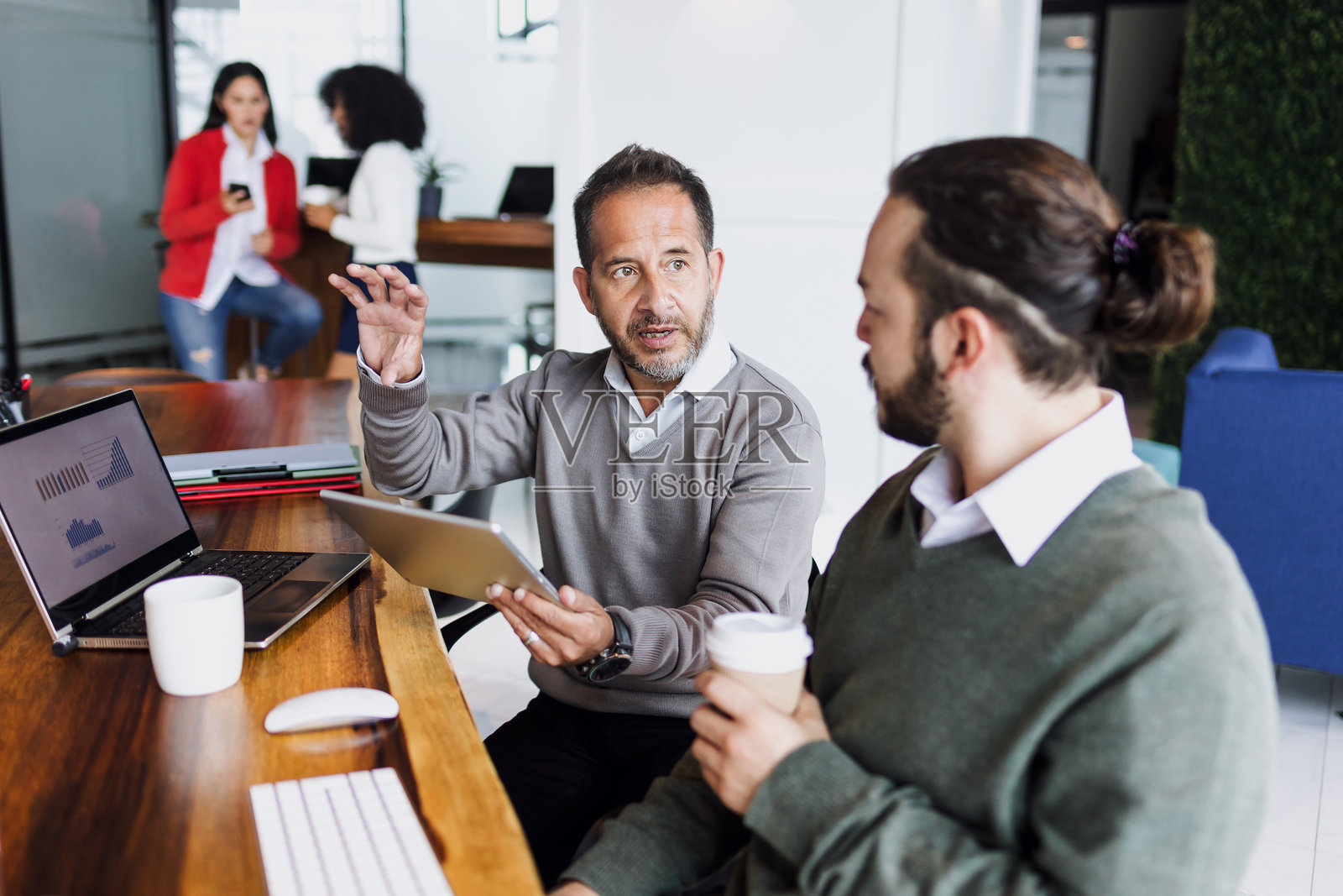 拉丁裔老年男性经理与年轻男性员工在墨西哥的创意办公室共同使用电脑,展现西班牙裔团队合作。照片摄影图片