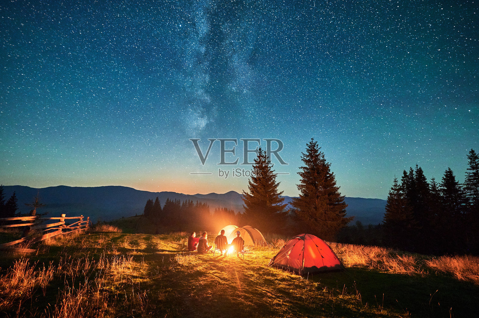 一群徒步旅行者围坐在篝火旁休息,周围是闪烁的帐篷和壮丽的星空。照片摄影图片