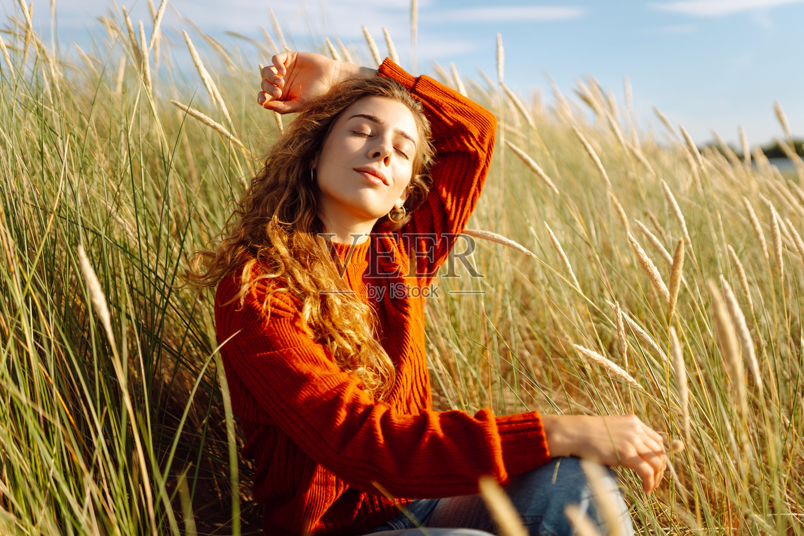 一位美丽的卷发女性在海滩的高草中享受阳光。照片摄影图片