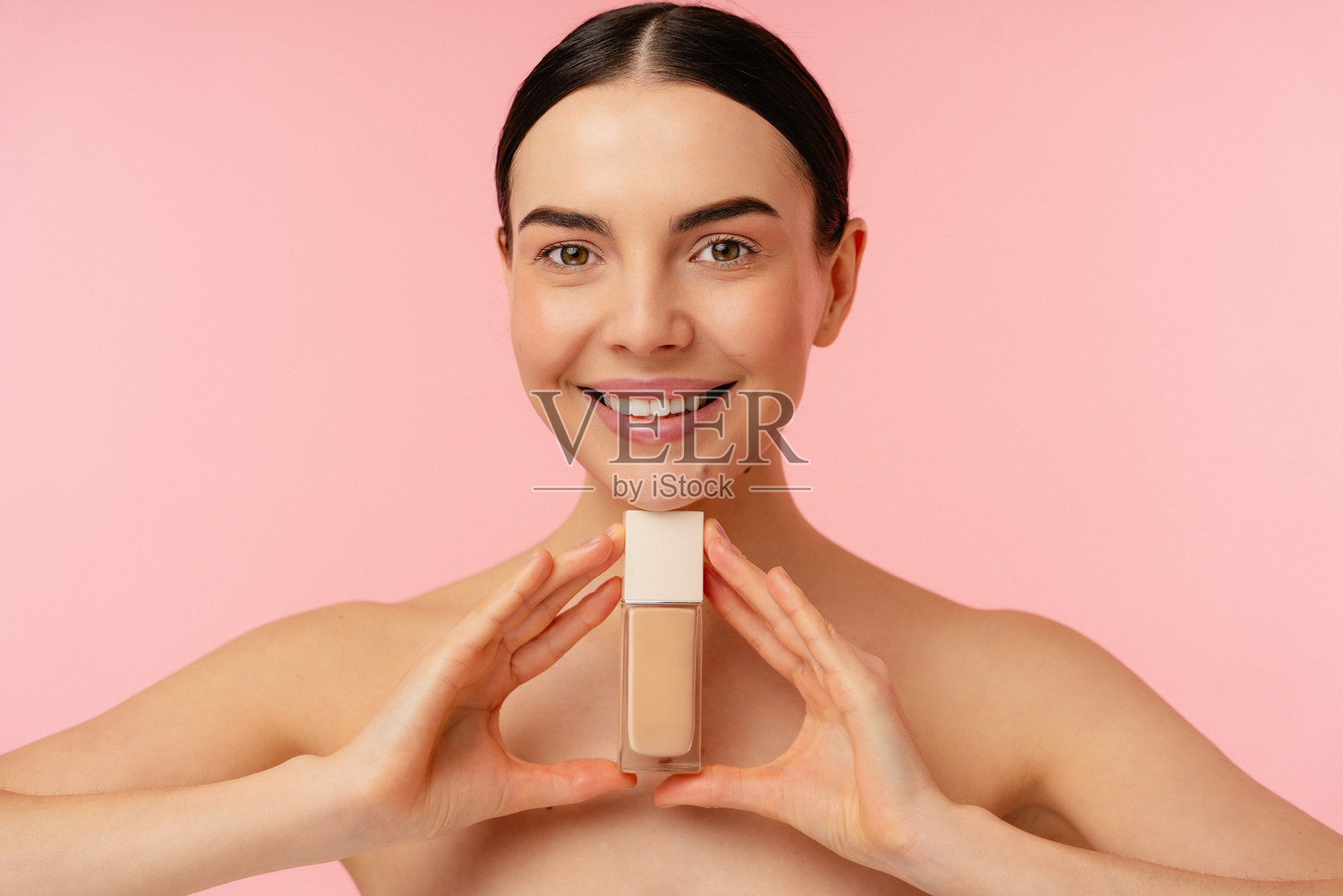 微笑的模特在粉色背景下展示粉底液瓶照片摄影图片