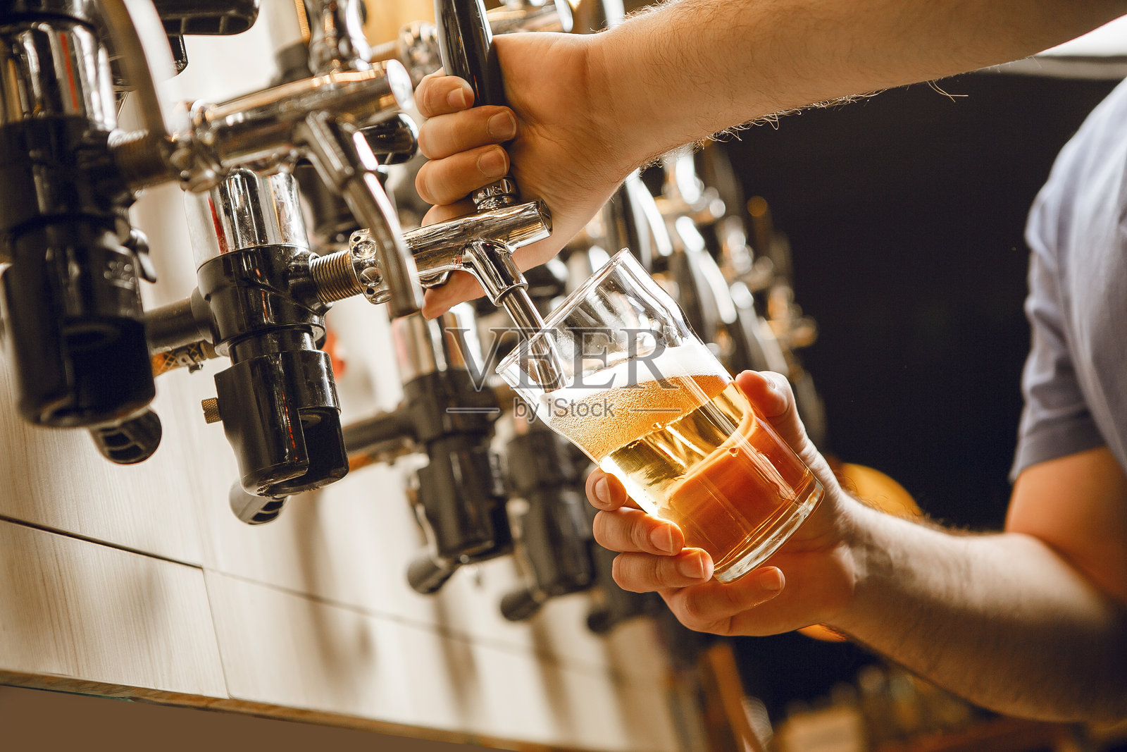 无脸人物在酒吧的水龙头上倒啤酒入杯,夜晚时分。照片摄影图片