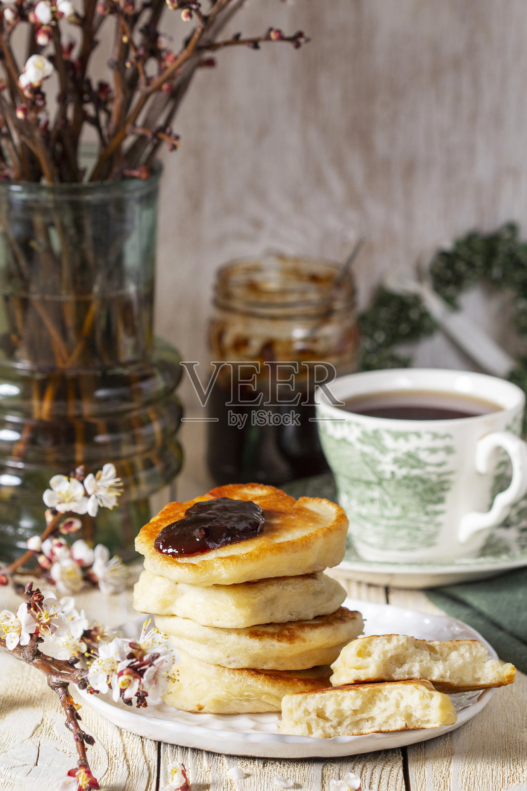 复活节酵母煎饼配梅子酱和茶,旁边是一束开花的杏树枝,摆放在浅色木桌上。照片摄影图片