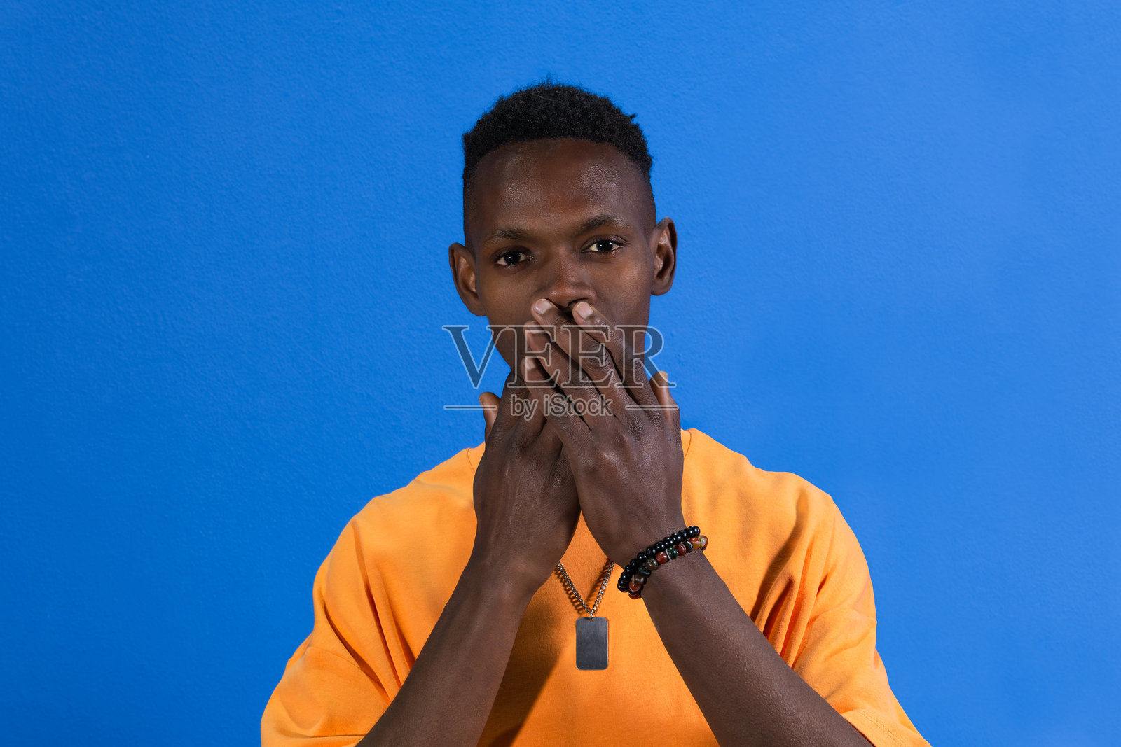 年轻的非洲男子在蓝色背景下捂住嘴巴照片摄影图片
