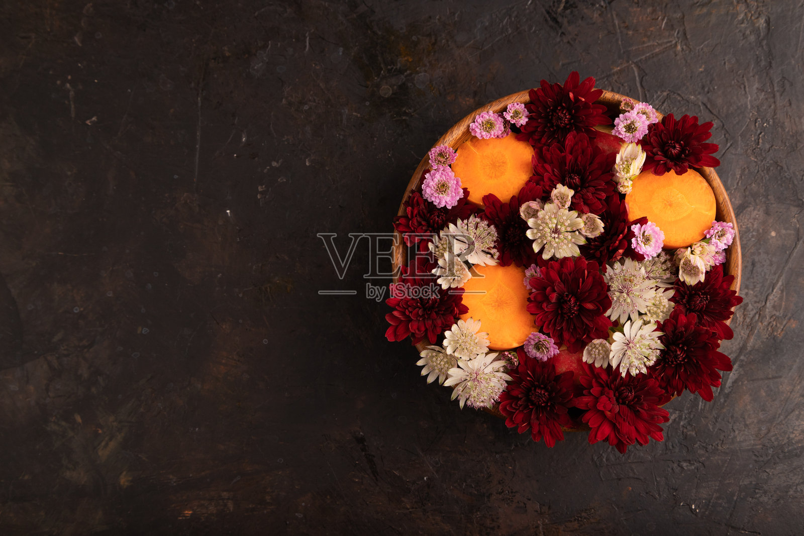 木碗里装着胡萝卜片和红色菊花、星辰花,黑色混凝土上的花卉沙拉,俯视图,留白空间照片摄影图片