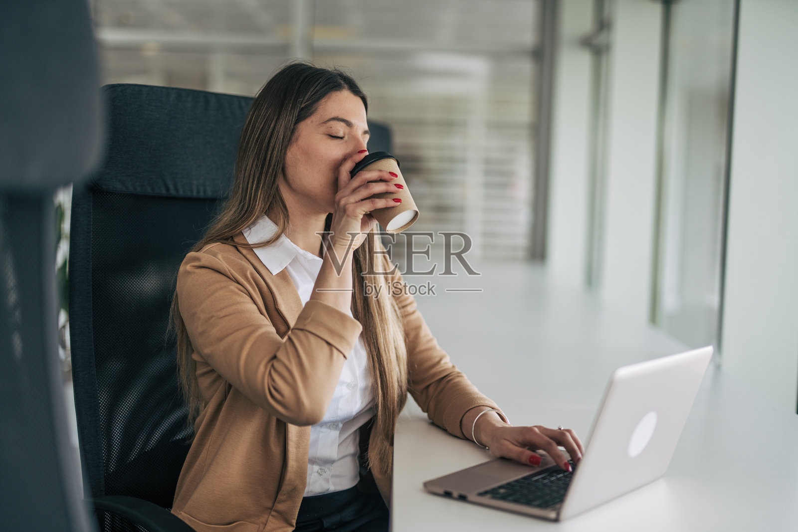 女商人在办公室喝咖啡,同时使用笔记本电脑工作照片摄影图片