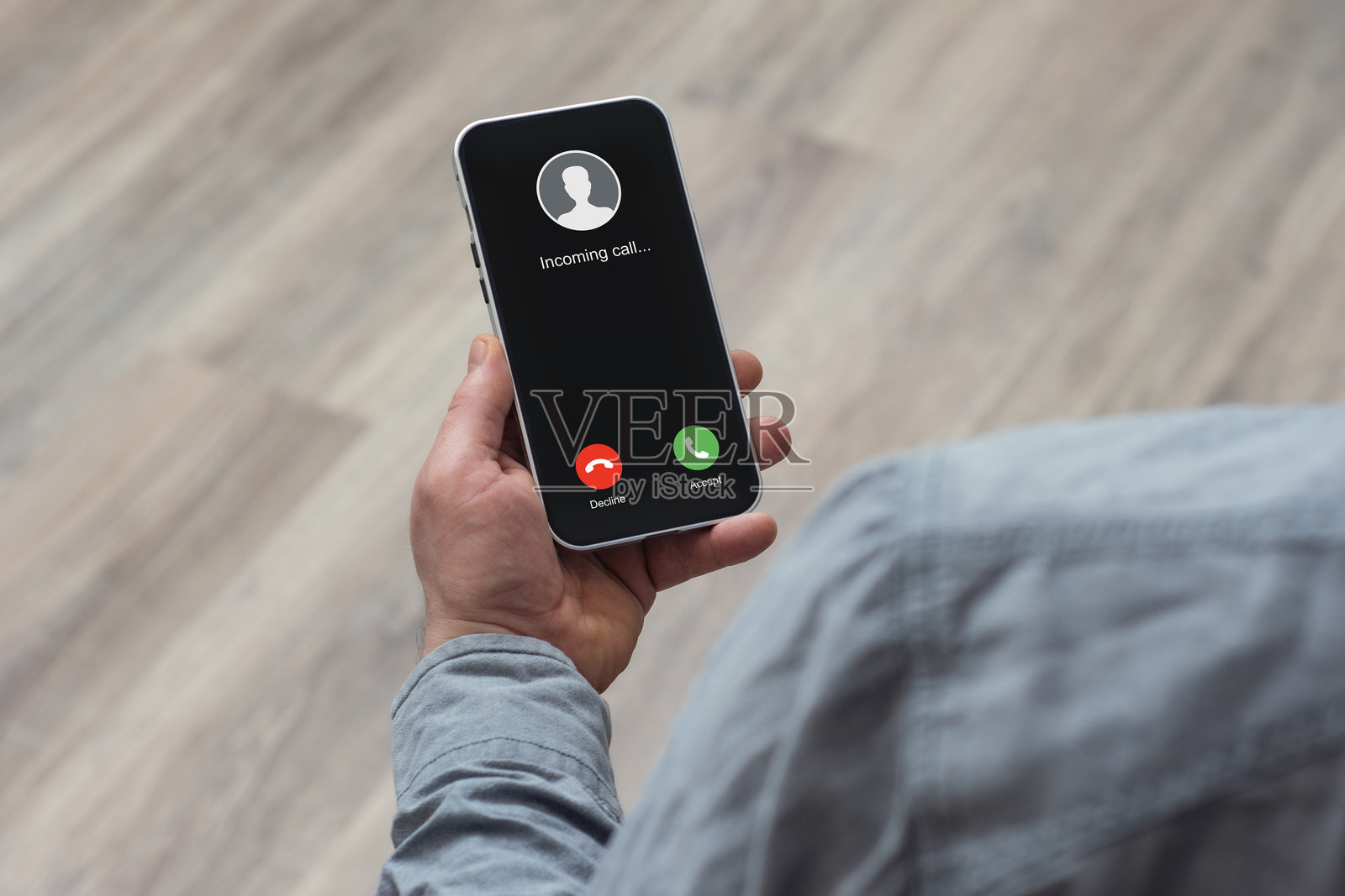 一个男人手持智能手机,屏幕上显示来电,背景是木地板。照片摄影图片