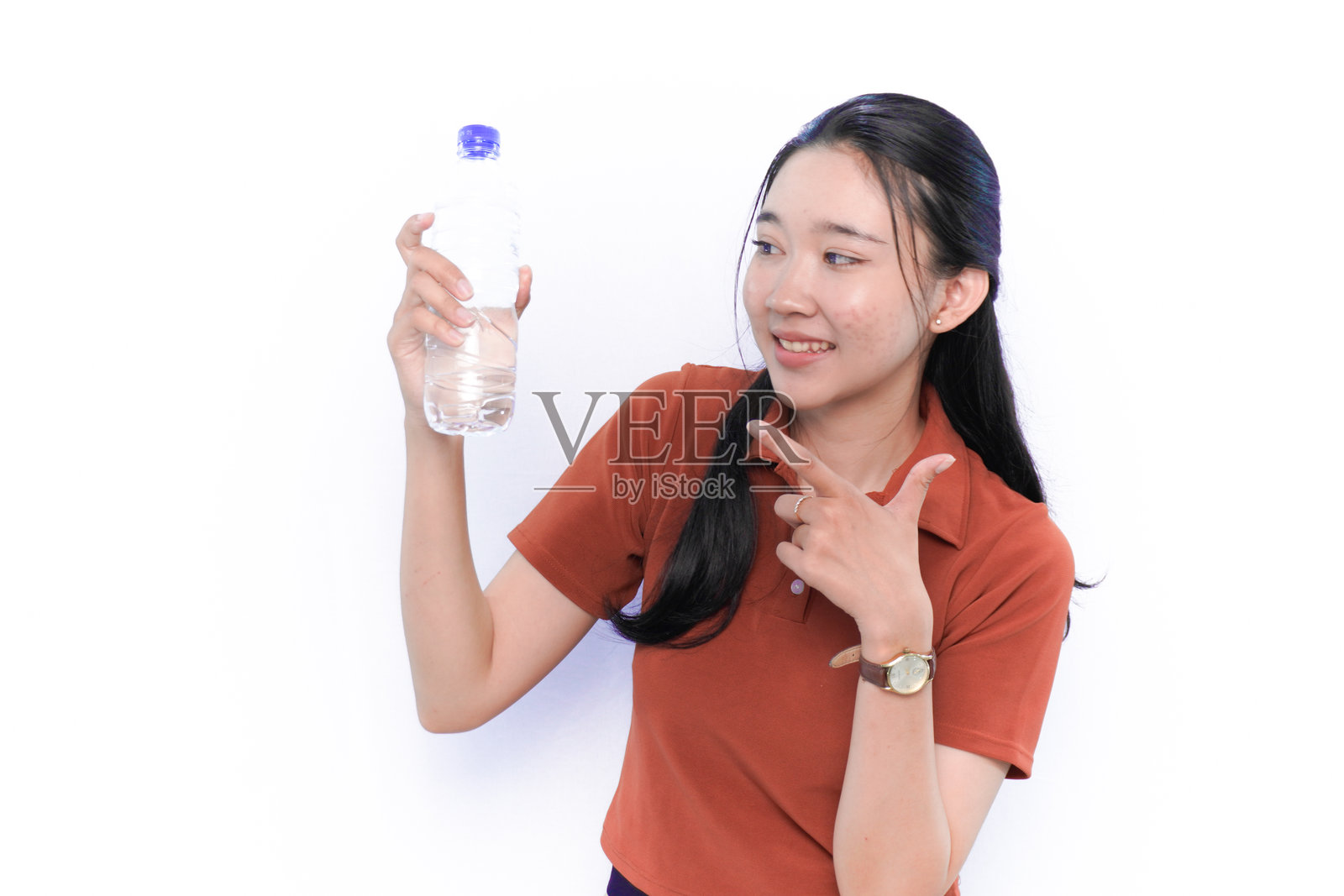 微笑的亚洲印尼模特穿着橙色连衣裙,手里拿着一瓶饮料。照片摄影图片