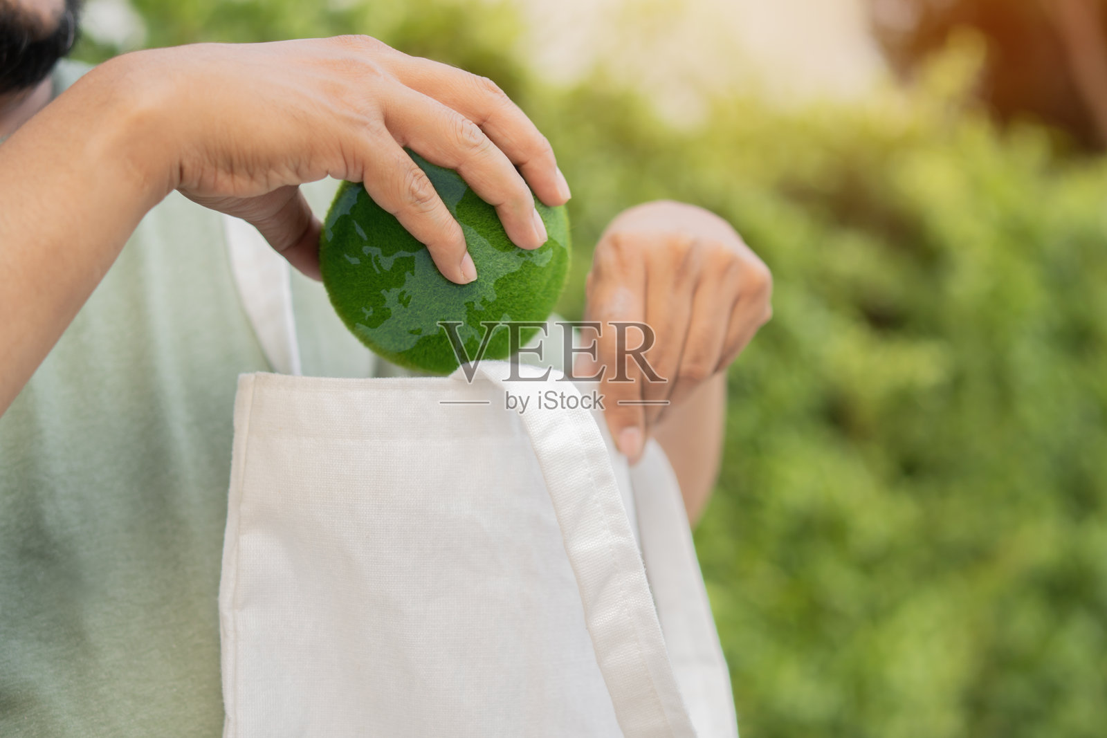 男子在户外将绿色地球球放入帆布袋中。照片摄影图片