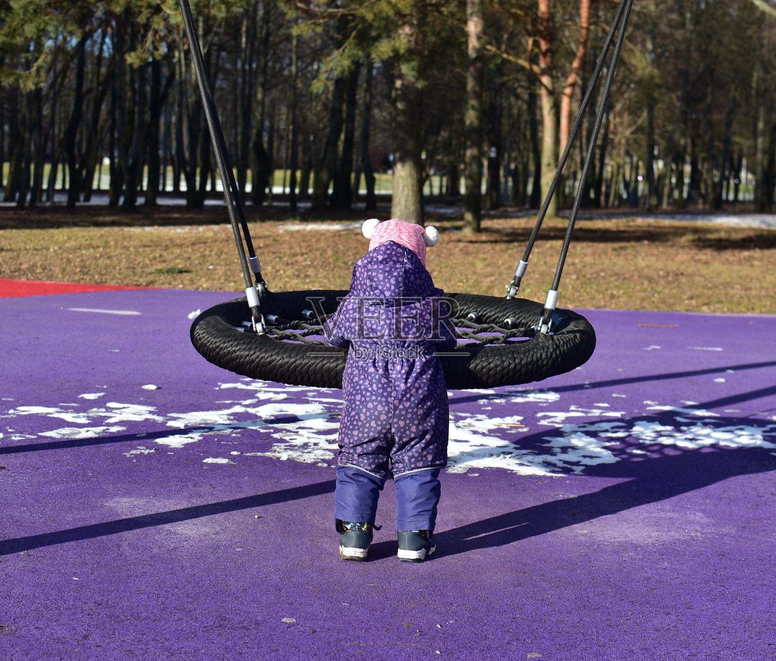 小女孩在城市公园的儿童游乐场里玩秋千,天气寒冷。幼儿女孩在冬季的公共游乐场里玩得很开心。照片摄影图片